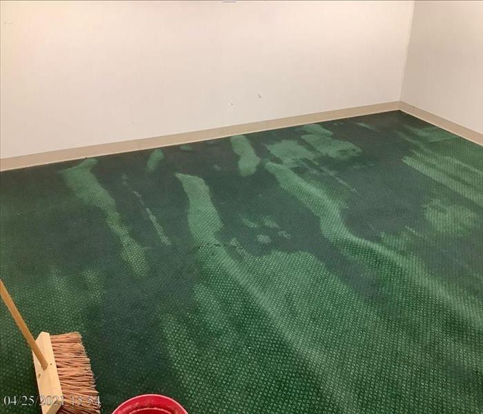 Green office carpet with water spots and push broom