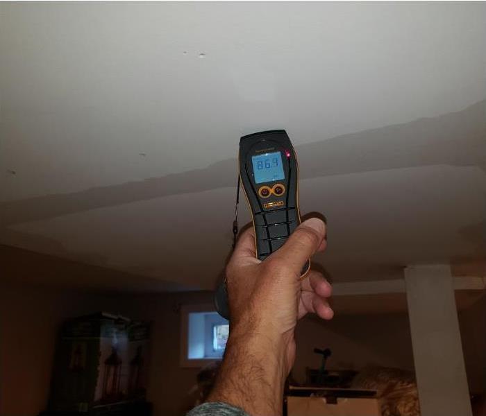 an employee holding a moisture meter on a water damaged ceiling